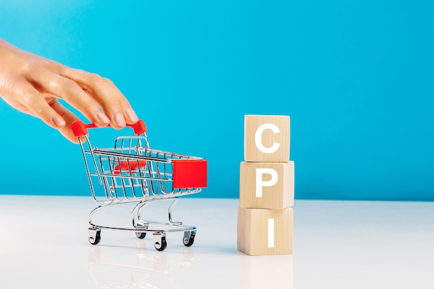 CPI-Verbraucherpreisindex-SymbolBuchstabenblock im Wort CPI-Abkürzung für Verbraucherpreisindex und Frauenhand, die leeren Einkaufswagen auf blauem Hintergrund drückt