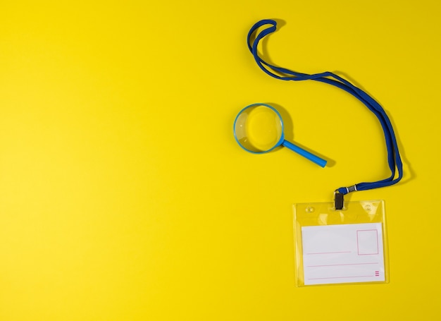 Crachá de plástico transparente em um cordão azul em um fundo amarelo, vista superior