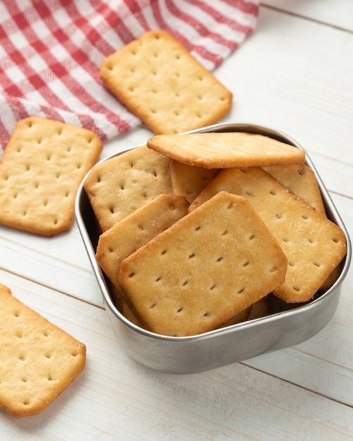 Cracker Cookies in einer Edelstahlschüssel mit Tischdecke auf weißem Holztisch Hintergrund.