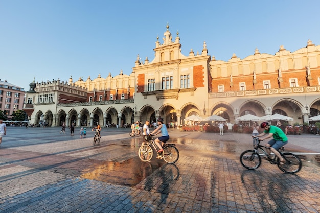 Foto cracóvia (polônia) 29 de junho de 2016 o salão do tecido polonês sukiennice pessoas andando de bicicleta na praça principal do mercado a antiga cidade medieval de cracôvia está listada como patrimônio da unesco