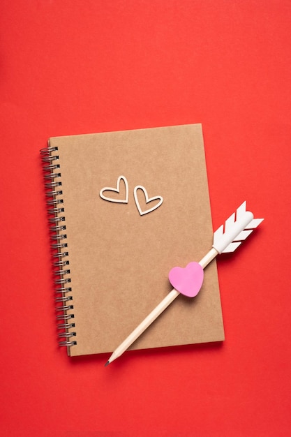 Craft Bloc de notas en blanco flecha pensil y corazones de madera sobre fondo rojo Mensaje de amor Día de San Valentín y concepto de vacaciones románticas Vista superior plana con espacio de copia