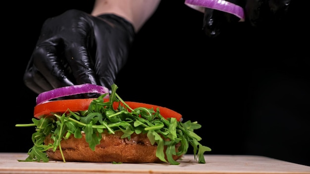 Craft Burger kocht auf schwarzem Hintergrund in schwarzen Lebensmittelhandschuhen