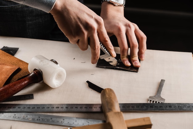 Craftsman está cortando cuero genuino usando un cuchillo cortador para crear productos de cuero natural Equipo para la producción de cuero genuino en el taller Proceso de corte de cuero genuino