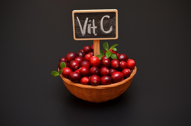 Cranberries frescas de frutas vermelhas e inscrição de vitamina C em um fundo escuro