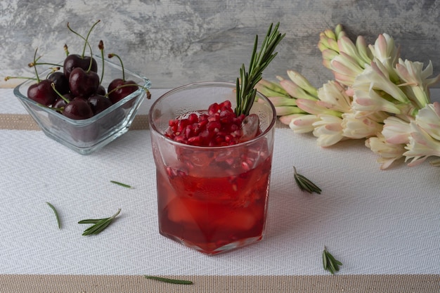 Cranberry-Drink mit Eisgranatapfel und Rosmarinzweig, begleitet von Kirschen und Blumen