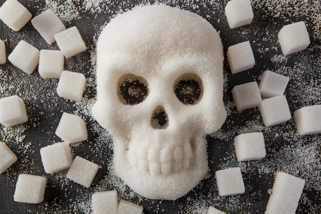 Foto cráneo de azúcar artístico entre cubos de azúcar en un fondo oscuro, una metáfora clara de los riesgos para la salud asociados con el consumo excesivo de azúcar