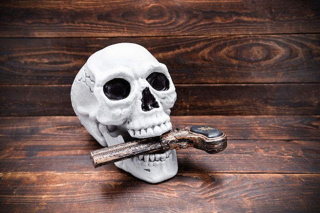 Cráneo humano con pistola tallada vintage en la boca sobre la superficie de la tabla de madera.
