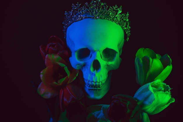 Foto crânio humano em uma coroa em flores de tulipa com iluminação neon colorida