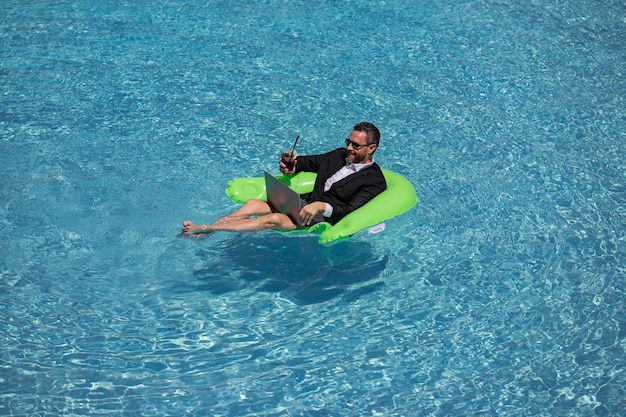 Crazy summer business beber cóctel de verano y usar una computadora portátil en traje en una piscina de agua divertida vida empresarial