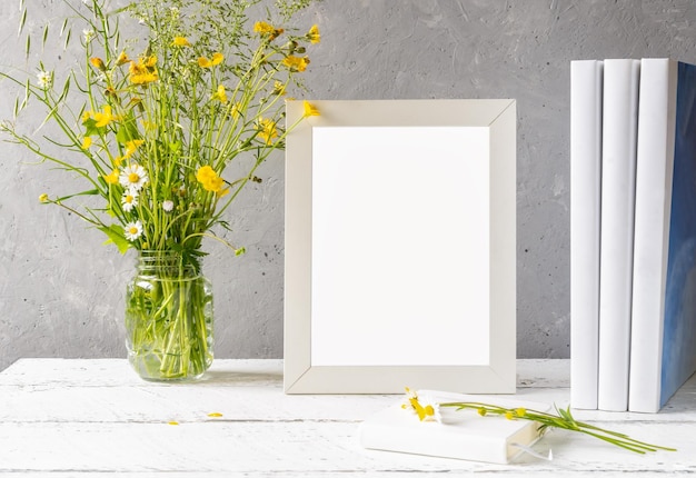 Creación de maquetas Marco blanco sobre mesa de madera blanca con fondo de hormigón gris y flores