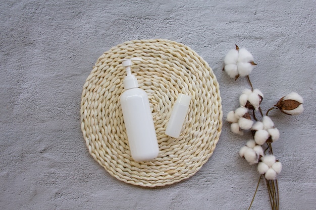 Foto creativo plano de botella de plástico con flores de algodón en almohadilla de mimbre