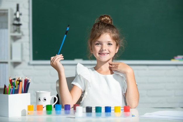 Crecimiento creativo de los niños Niña dibuja en el aula sentada en una mesa divirtiéndose en la escuela blackboar