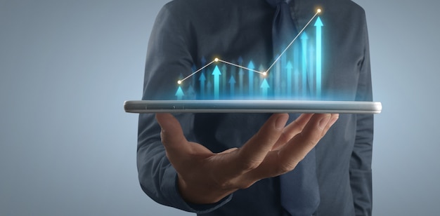 Crecimiento del gráfico del plan de empresario y aumento de los indicadores positivos del gráfico en su negocio, tableta en mano