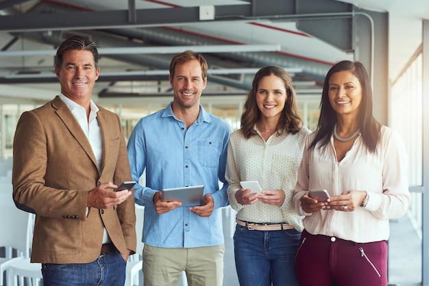 Creen en una fuerte presencia en línea Retrato de un equipo de empresarios posando con sus dispositivos inalámbricos en la oficina