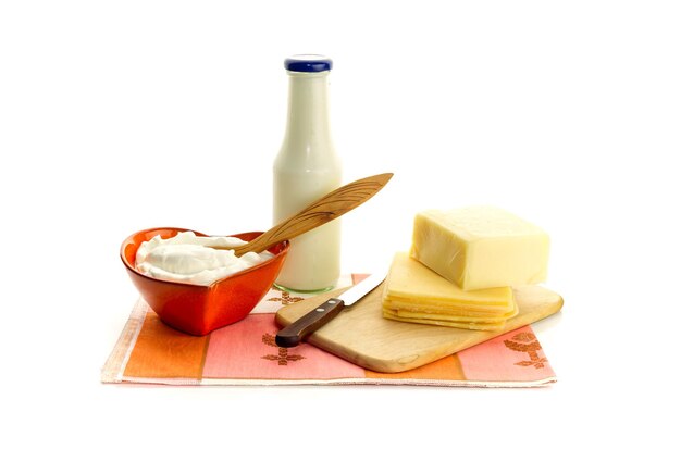 Crema agria láctea en un tazón de queso y leche en una botella sobre un fondo blanco cerrado