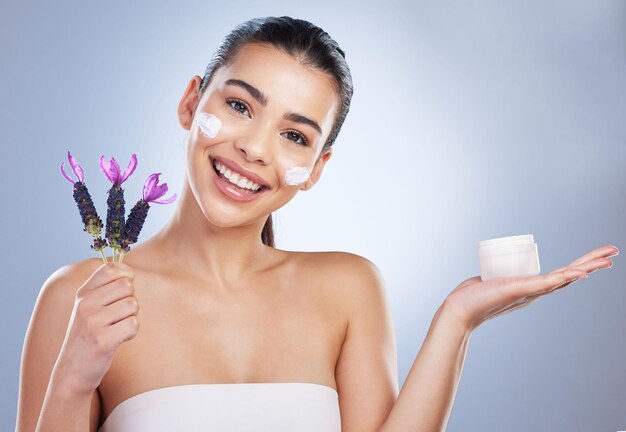 Foto crema de belleza y mujer con flor de lavanda en estudio para productos para el cuidado de la piel y brillo natural retrato de modelo femenino feliz sobre un fondo degradado para cosméticos de brillo facial y humectante facial