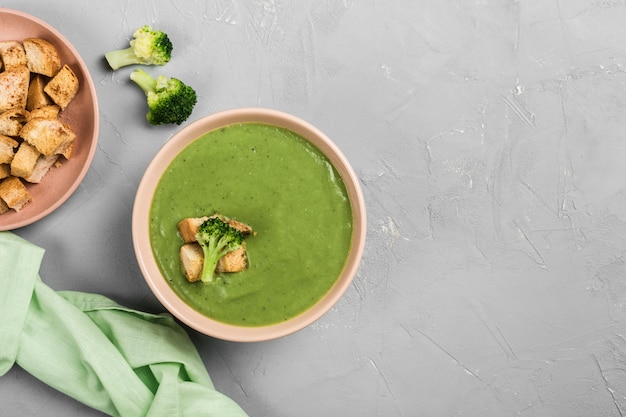 Crema de brócoli con picatostes en un plato y una servilleta verde sobre un fondo gris claro. Concepto de nutrición saludable.