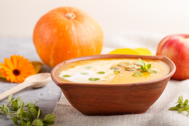 Crema de calabaza tradicional con semillas en un recipiente de arcilla sobre un fondo de hormigón gris con lino textil