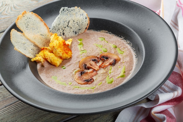 Crema de champiñones en un tazón oscuro, sopa cremosa casera con champiñones en rodajas.