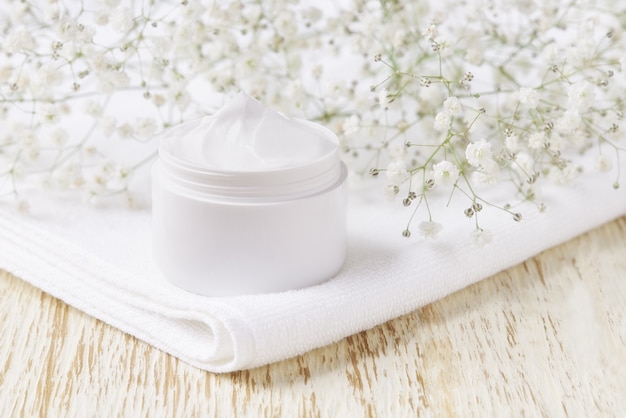 Crema cosmética herbal curativa, producto higiénico para el cuidado de la piel o mascarilla de maquillaje relajante en un frasco de plástico con una toalla sobre una mesa de madera.