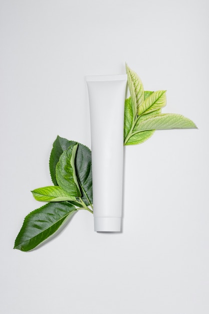 Crema cosmética para hidratar y limpiar el rostro. Crema o mascarilla en tubos blancos y hojas de plantas naturales. Botella blanca con espacio vacío