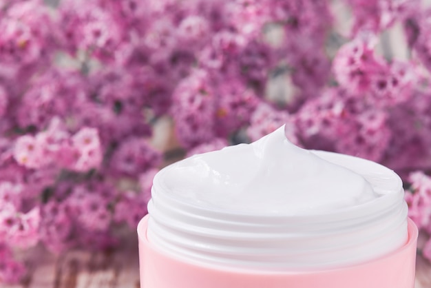 Crema cosmética saludable con cuidado facial a base de hierbas o loción humectante, de cerca. Tarro de plástico rosa para crema para pieles sensibles en una mesa de madera.