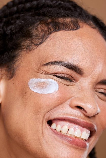 Foto crema para el cuidado de la piel y la cara de una mujer emocionada por un producto de belleza contra un fondo marrón de estudio protector solar feliz y modelo de niña con una sonrisa para dermatología de crema facial y zoom en brillo