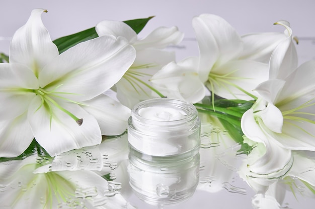 Crema para el cuidado de la piel, cosmética natural a base de flores y pétalos. Un frasco de vidrio con crema blanca se encuentra entre las flores de lirio