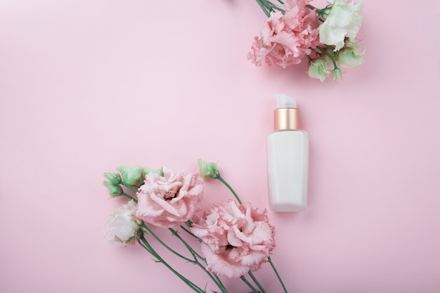Crema facial con flores frescas de color rosa y blanco, flatlay sobre fondo rosa con mucho espacio para copiar. Concepto cosmético para el cuidado de la piel y el envejecimiento.