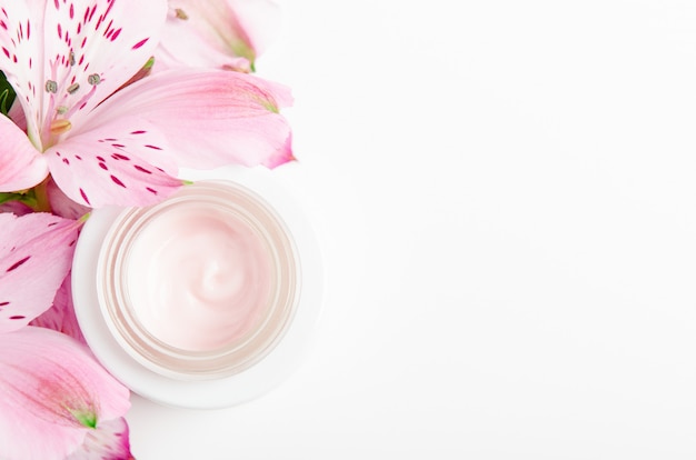 Crema facial en frasco blanco con flores rosas.