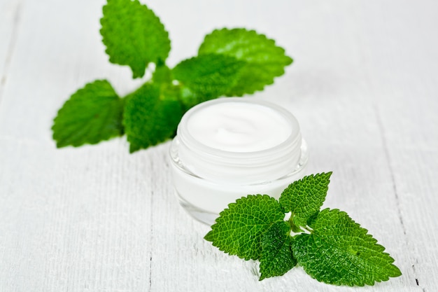 Crema facial en frasco de vidrio con hojas verdes de urtica.