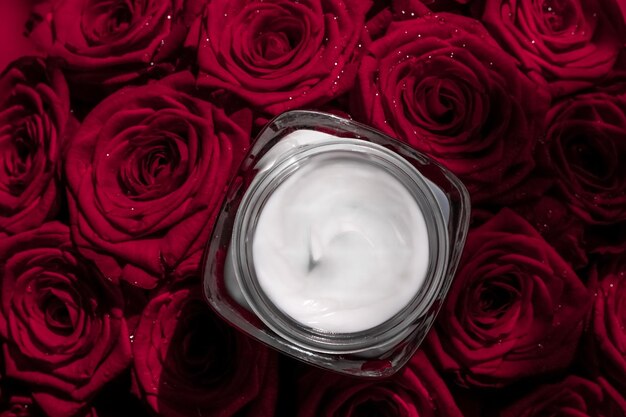 Crema facial hidratante para la piel y flores de rosas rojas producto cosmético de lujo para el cuidado de la piel sobre fondo floral como diseño plano de vacaciones de la marca de belleza