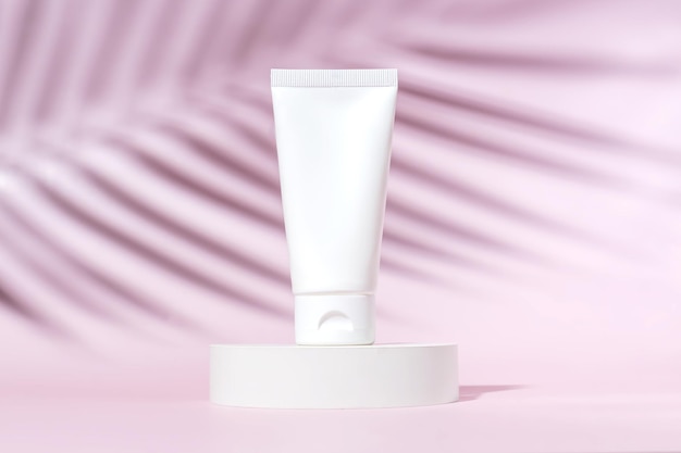 Crema facial o de manos en un tubo de plástico blanco sobre un fondo rosa con la sombra de una palmera tropical Accesorio cosmético femenino para maquillaje Espacio de copia de identidad de maqueta