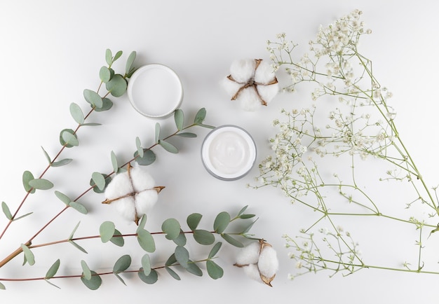 Crema facial sobre la mesa con eucalipto y algodón.