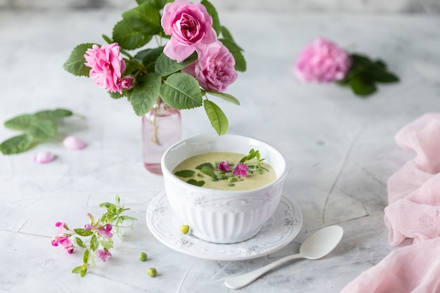 Crema de guisantes verdes sobre un fondo de mármol blanco con un ramo de rosas