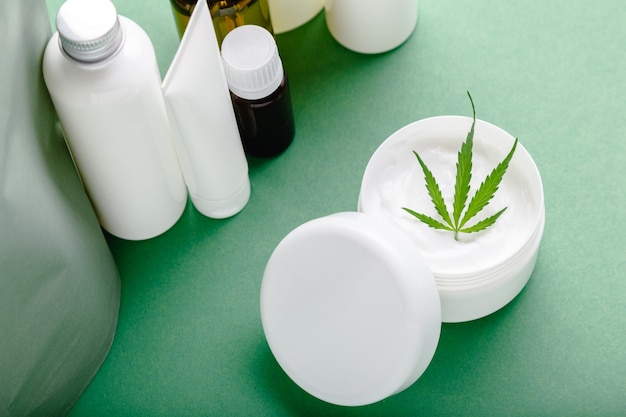 Crema hidratante de cáñamo en frasco blanco con aceite de CBD hoja de cannabis y cosméticos para el cuidado de la piel sobre fondo verde