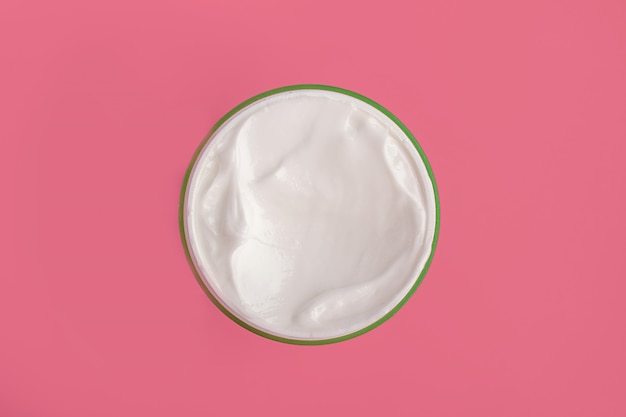 Crema hidratante cosmética de cara blanca en un frasco redondo sobre un fondo rosa. Plano pone macro aislado.