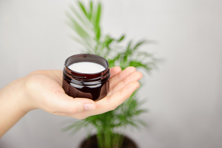 Crema hidratante de manteca de karité para el cuidado de la piel y el cabello. Mano que sostiene la crema cosmética orgánica natural en el tarro.