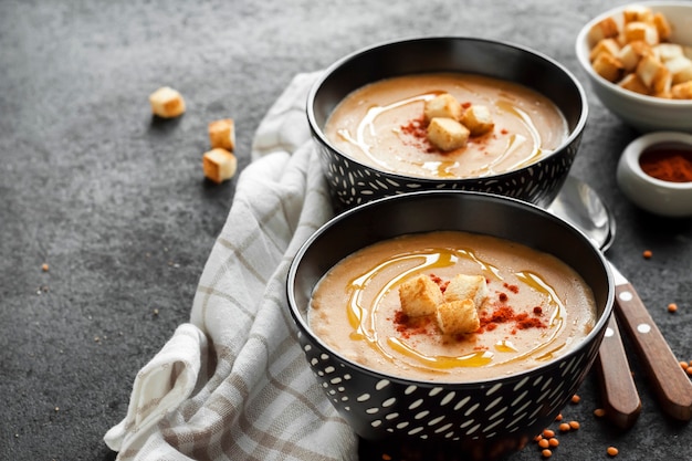 Crema de lentejas con pimentón y picatostes en cuencos de cerámica negra sobre fondo oscuro. Copia espacio