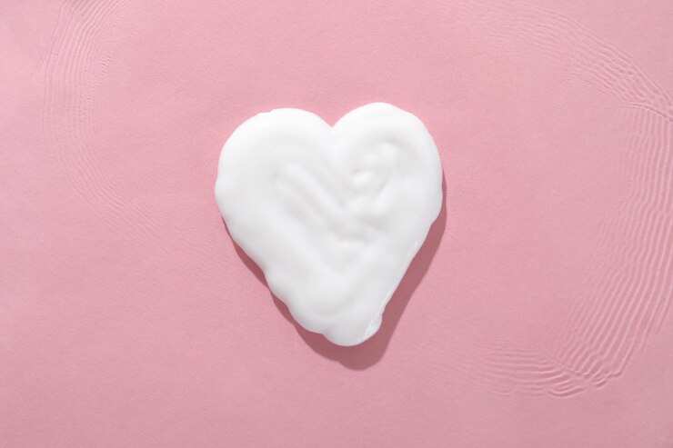 Crema de manos en forma de corazón, primer plano, sobre fondo rosa.