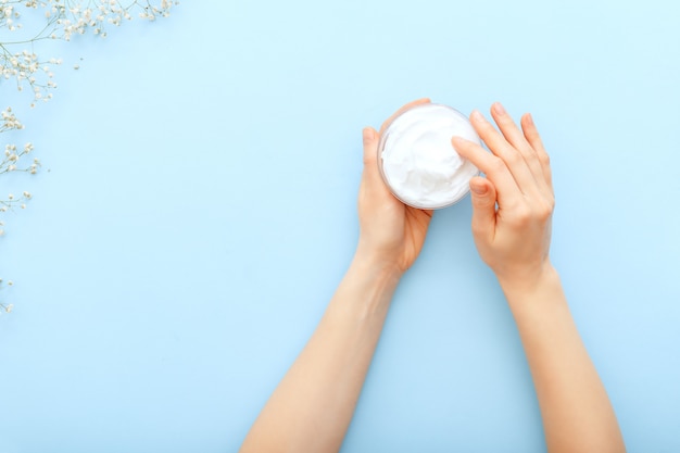 Crema de manos, manos femeninas aplicando cosméticos naturales crema orgánica sobre un fondo de color azul pastel. Crema para el cuidado de la piel en frasco para manos, cuerpo. Crema hidratante plana para piel suave, salud, belleza.