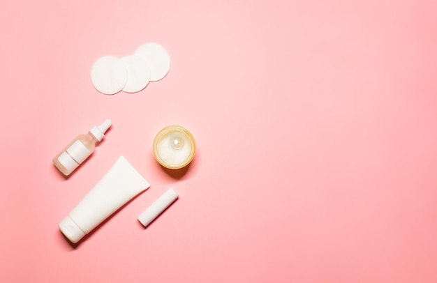 crema de manos en un tubo blanco aceite esencial bálsamo labial almohadillas de algodón y una vela sobre fondo rosa pastel