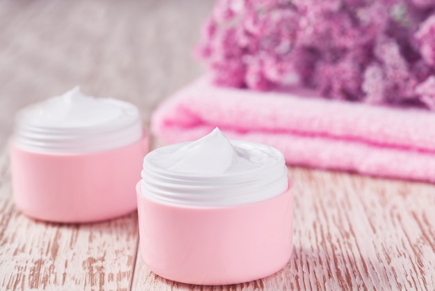 Crema o loción facial natural, producto cosmético orgánico para hidratar la piel con toalla y flores de fondo. Cosmético de la serie rosa.