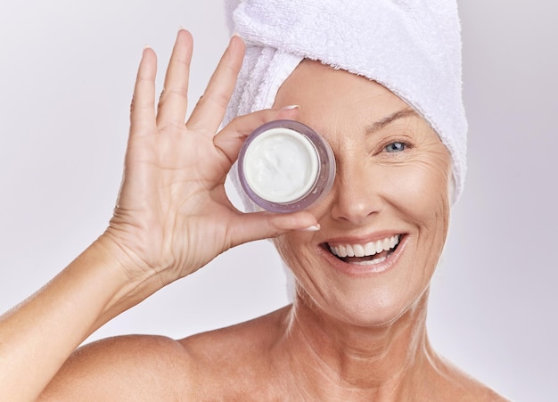 Foto crema de retrato y belleza con anciana feliz con cuidado de la piel y dermatología sobre fondo blanco crema hidratante con protector solar y cuidado facial modelo femenino aplicar loción con recipiente de vidrio y piel