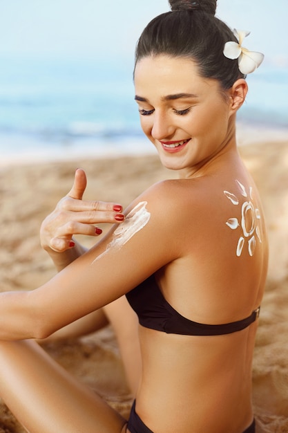 Crema solar Cuidado de la piel y el cuerpo. Mujer en Bikini aplicando protector solar solar en el hombro bronceado.