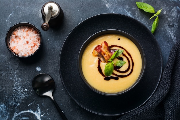 Crema de sopa de patata con tocino y salsa de soja en un tazón negro, sobre una superficie de hormigón antiguo oscuro