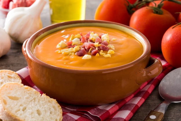 Crema típica de salmorejo español con jamón y huevo sobre mesa de madera