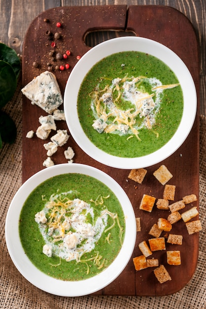 Crema verde de espinacas y brócoli. con la adición de parmesano y queso azul con picatostes. Una superficie de madera.