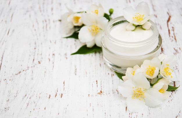 Cremas hidratantes de cara y cuerpo con flores de jazmín sobre fondo de madera blanco