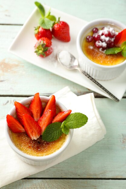 Crème Brûlée Dessert mit frischen Erdbeerbeeren auf Serviette auf farbigem Holzhintergrund